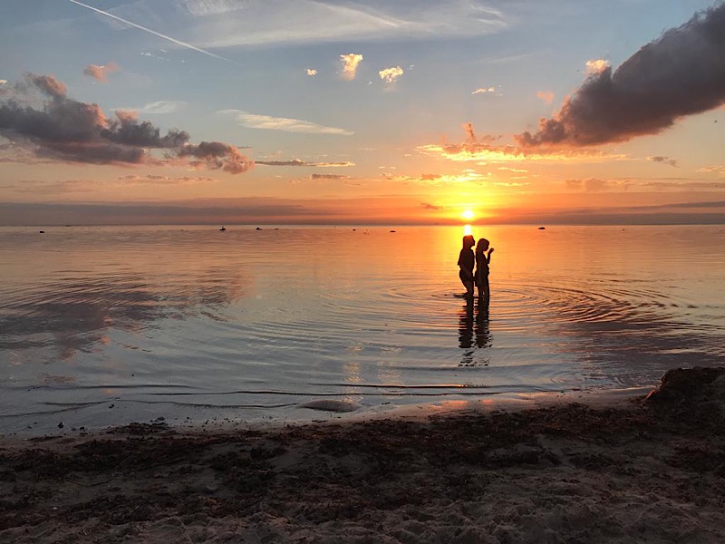 Zwei Kinder stehen im Meer im Sonnenuntergang